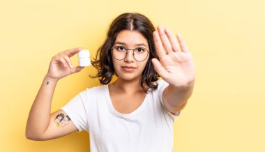 Genç İspanyol kadın ciddi görünüyor. Avuç içini gösteriyor. Durdurma hareketi yapıyor. hastalık hapları konsepti