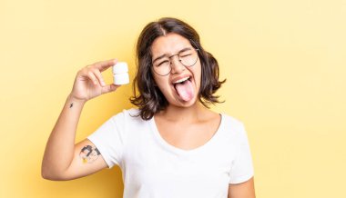 Neşeli ve asi tavırları olan, şaka yapan ve dilini dışarı çıkaran genç İspanyol bir kadın. hastalık hapları konsepti