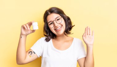 Genç İspanyol kadın mutlu bir şekilde gülümsüyor, el sallıyor, sizi selamlıyor ve selamlıyor. hastalık hapları konsepti