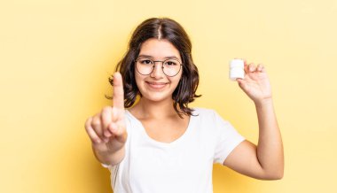 Genç İspanyol kadın gülümsüyor ve arkadaş canlısı görünüyor, bir numarayı gösteriyor. hastalık hapları konsepti