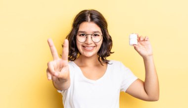 Genç İspanyol kadın gülümsüyor ve arkadaş canlısı görünüyor, iki numarayı gösteriyor. hastalık hapları konsepti