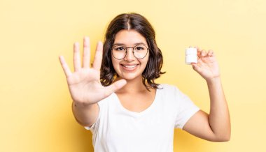 Genç İspanyol kadın gülümsüyor ve arkadaş canlısı görünüyor, beş numarayı gösteriyor. hastalık hapları konsepti