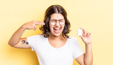 Genç İspanyol kadın mutsuz ve stresli görünüyor, intihar jesti silah işareti yapıyor. hastalık hapları konsepti