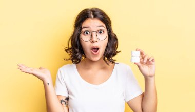 Genç İspanyol kadın şaşırmış ve şok olmuş görünüyor. Çenesi düşmüş ve elinde bir nesne tutuyor. hastalık hapları konsepti