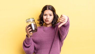 Latin kökenli genç bir kadın kızmış, baş parmağını kaldırmış. kahve çekirdeği konsepti