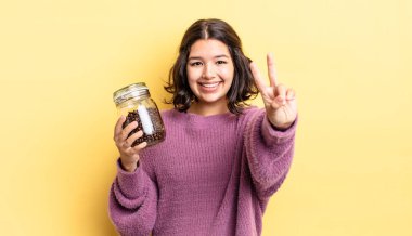 Genç İspanyol kadın gülümsüyor ve arkadaş canlısı görünüyor, iki numarayı gösteriyor. kahve çekirdeği konsepti