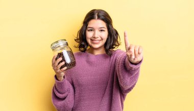 Genç İspanyol kadın gülümsüyor ve arkadaş canlısı görünüyor, bir numarayı gösteriyor. kahve çekirdeği konsepti