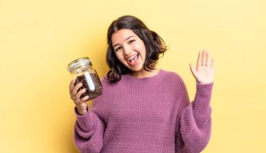 Genç İspanyol kadın mutlu bir şekilde gülümsüyor, el sallıyor, sizi selamlıyor ve selamlıyor. kahve çekirdeği konsepti