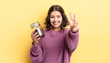 Genç İspanyol kadın gülümsüyor ve arkadaş canlısı görünüyor, üç numarayı gösteriyor. kahve çekirdeği konsepti