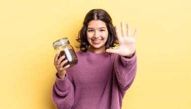 Genç İspanyol kadın gülümsüyor ve arkadaş canlısı görünüyor, beş numarayı gösteriyor. kahve çekirdeği konsepti