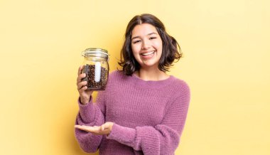 Genç İspanyol kadın neşeyle gülümsüyor, mutlu hissediyor ve bir konsept gösteriyor. kahve çekirdeği konsepti