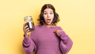 Genç İspanyol kadın şok olmuş ve ağzı açık, kendini işaret ederek şaşırmış görünüyor. kahve çekirdeği konsepti