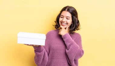 Genç İspanyol kadın mutlu ve kendinden emin bir ifadeyle gülümsüyor. Elleri çenesinde. boş kutu kavramı