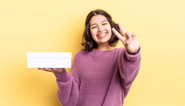 Genç İspanyol kadın gülümsüyor ve mutlu görünüyor, zafer ya da barış işareti yapıyor. boş kutu kavramı