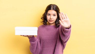 Genç İspanyol kadın ciddi görünüyor. Avuç içini gösteriyor. Durdurma hareketi yapıyor. boş kutu kavramı