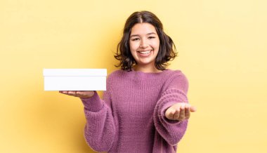 Genç İspanyol kadın mutlu bir şekilde gülümsüyor ve bir konsept sunuyor. boş kutu kavramı