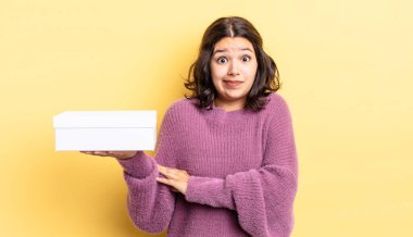 Genç İspanyol kadın omuz silkiyor, kafası karışık ve kararsız. boş kutu kavramı