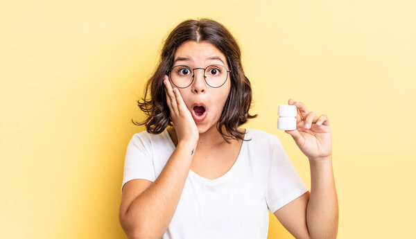 young hispanic woman feeling shocked and scared. illness pills concept