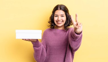 Genç İspanyol kadın gülümsüyor ve arkadaş canlısı görünüyor, iki numarayı gösteriyor. boş kutu kavramı