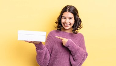 Genç İspanyol kadın neşeyle gülümsüyor, mutlu hissediyor ve bir tarafı işaret ediyor. boş kutu kavramı