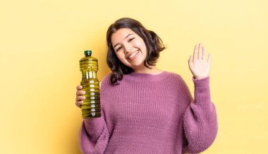 Genç İspanyol kadın mutlu bir şekilde gülümsüyor, el sallıyor, sizi selamlıyor ve selamlıyor. Zeytin yağı kavramı