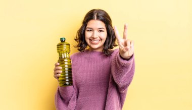 Genç İspanyol kadın gülümsüyor ve arkadaş canlısı görünüyor, iki numarayı gösteriyor. Zeytin yağı kavramı