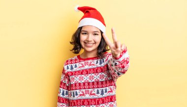 Genç İspanyol kadın gülümsüyor ve arkadaş canlısı görünüyor, iki numarayı gösteriyor. Noel konsepti