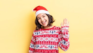 Genç İspanyol kadın mutlu bir şekilde gülümsüyor, el sallıyor, sizi selamlıyor ve selamlıyor. Noel konsepti