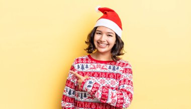 Genç İspanyol kadın neşeyle gülümsüyor, mutlu hissediyor ve bir tarafı işaret ediyor. Noel konsepti