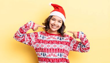 Genç İspanyol kadın kendine güvenerek gülümsüyor ve kendi gülüşünü gösteriyor. Noel konsepti