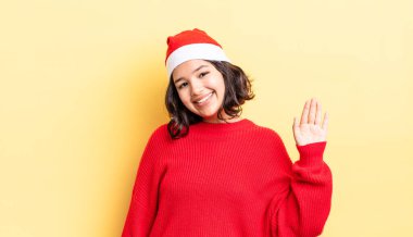 Genç İspanyol kadın mutlu bir şekilde gülümsüyor, el sallıyor, sizi selamlıyor ve selamlıyor. Noel konsepti