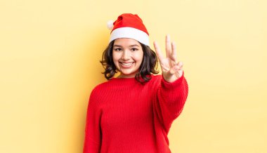 Genç İspanyol kadın gülümsüyor ve arkadaş canlısı görünüyor, üç numarayı gösteriyor. Noel konsepti