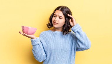 Genç İspanyol kadın mutlu bir şekilde gülümsüyor ve hayal kuruyor ya da şüphe ediyor. boş kase kavramı