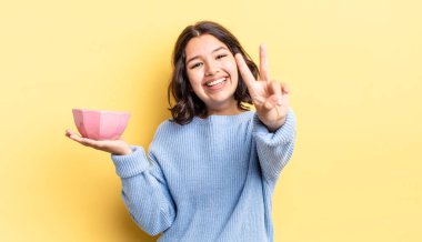 Genç İspanyol kadın gülümsüyor ve mutlu görünüyor, zafer ya da barış işareti yapıyor. boş kase kavramı