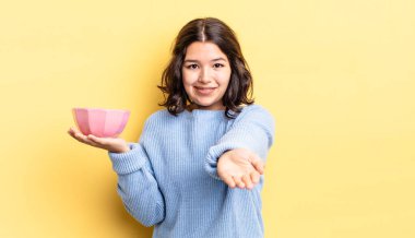 Genç İspanyol kadın mutlu bir şekilde gülümsüyor ve bir konsept sunuyor. boş kase kavramı