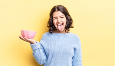 Neşeli ve asi tavırları olan, şaka yapan ve dilini dışarı çıkaran genç İspanyol bir kadın. boş kase kavramı