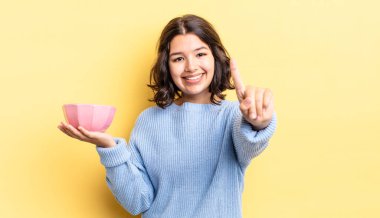 Genç İspanyol kadın gülümsüyor ve arkadaş canlısı görünüyor, bir numarayı gösteriyor. boş kase kavramı