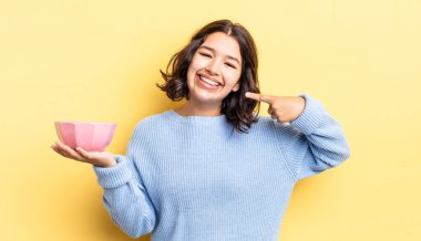 Genç İspanyol kadın kendine güvenerek gülümsüyor ve kendi gülüşünü gösteriyor. boş kase kavramı