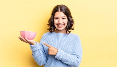 Genç İspanyol kadın neşeyle gülümsüyor, mutlu hissediyor ve bir tarafı işaret ediyor. boş kase kavramı