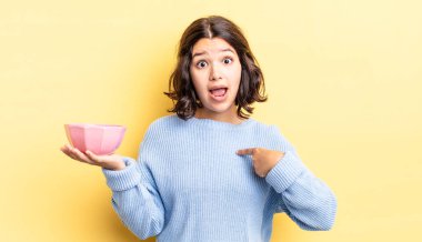 Genç İspanyol kadın şok olmuş ve ağzı açık, kendini işaret ederek şaşırmış görünüyor. boş kase kavramı