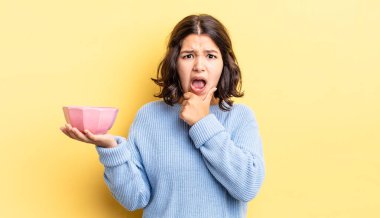 Ağzı ve gözleri sonuna kadar açık ve eli çenesinde olan genç İspanyol kadın. boş kase kavramı