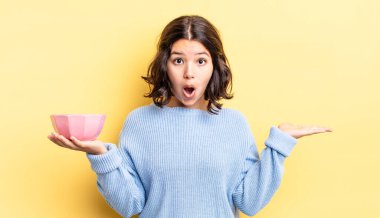 Genç İspanyol kadın şaşırmış ve şok olmuş görünüyor. Çenesi düşmüş ve elinde bir nesne tutuyor. boş kase kavramı