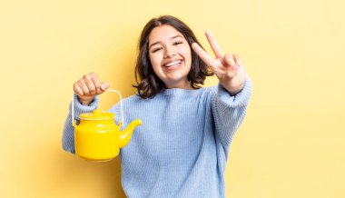 Genç İspanyol kadın gülümsüyor ve mutlu görünüyor, zafer ya da barış işareti yapıyor. çaydanlık konsepti