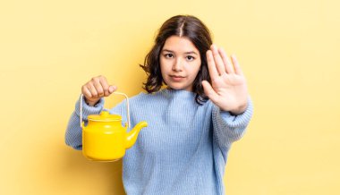 Genç İspanyol kadın ciddi görünüyor. Avuç içini gösteriyor. Durdurma hareketi yapıyor. çaydanlık konsepti