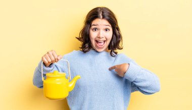 Genç İspanyol kadın kendini mutlu hissediyor ve heyecanla kendini işaret ediyor. çaydanlık konsepti