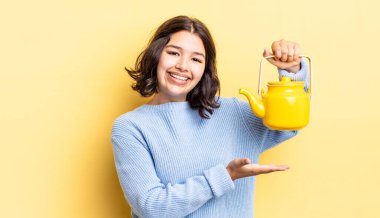 Genç İspanyol kadın neşeyle gülümsüyor, mutlu hissediyor ve bir konsept gösteriyor. çaydanlık konsepti