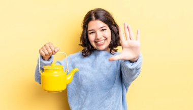 Genç İspanyol kadın gülümsüyor ve arkadaş canlısı görünüyor, beş numarayı gösteriyor. çaydanlık konsepti