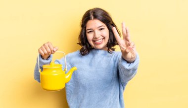 Genç İspanyol kadın gülümsüyor ve arkadaş canlısı görünüyor, üç numarayı gösteriyor. çaydanlık konsepti