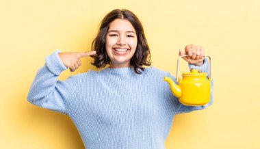 Genç İspanyol kadın kendine güvenerek gülümsüyor ve kendi gülüşünü gösteriyor. çaydanlık konsepti