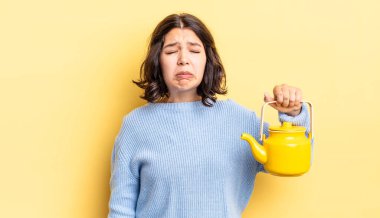 Genç İspanyol kadın üzgün ve mızmızlanıyor. Mutsuz bir bakışı var ve ağlıyor. çaydanlık konsepti